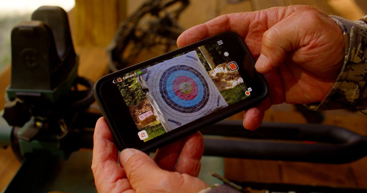 Close-up of a hunter viewing an archery target in the Longshot app on a phone beside a Longshot receiver
